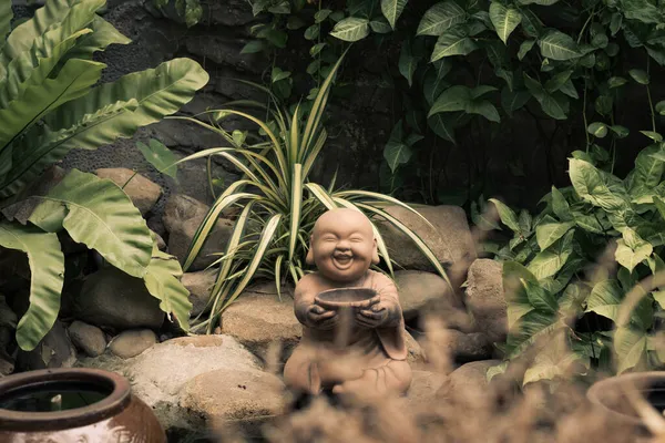 E Statuette figurine symbol brown stone buddha smile hold bowl. Copy space nature tropical leaves plants garden. Mysterious calm soul meditation mood buddhist culture. Bright green, more tone in stock — Stock Photo, Image