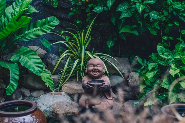 E Patung simbol batu coklat Buddha memegang mangkuk tersenyum. Salin alam tropis meninggalkan kebun tanaman. Misterius tenang jiwa meditasi suasana hati Buddha budaya. Hijau terang, lebih banyak nada dalam stok — Stok Foto
