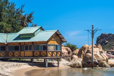 Doğa manzaralı arka plan. Güneş günü mavi gökyüzü ağacı koyunda kum kıyısında büyük bir kaya var. Ahşap yapışkan su yazlık evin pencere pervazı çatı. Eski lastikler salıncak. Tatil aşkı basit, sakin bir hayat sürüyor. 