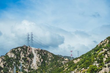 Gerçek doğa güzelliği arka planı. Rocky dağı, parlak bulutlu mavi gökyüzü yaz günü, yüksek voltajlı elektrik direkleri. Güneş ruh hali. Güç kaynağı uzak alanlar, mühendislik yapıları