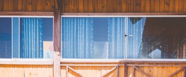 Dış görünüş. Tahta sarısı kahverengi tahta kumaş, kır evi, panoramik pencere camı yansıması, perdeler içeri. Yaz günü sıcak hava. Konforlu ev içleri, boş zaman, ekoloji binası