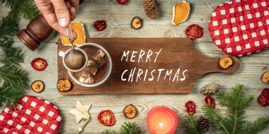 Elin tarçınlı sıcak çikolatayı bir fincana marşmelov serpiyor. Kesme tahtasının üzerinde Mutlu Noeller yazılıydı ve masanın etrafında da şenlikli aksesuarlar vardı. Tatil havası kavramı