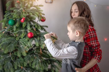 Anne ve çocuğu Noel ağacını oyuncaklar ve toplarla süslüyorlar. Yeni yıla aile hazırlığı, rahat atmosfer ve şenlik havası kavramı.