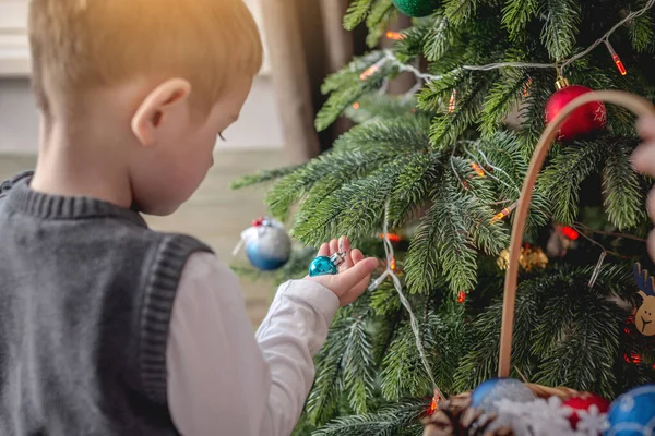 かわいい男の子はおもちゃやボールでクリスマスツリーを飾ることです 新年の準備の概念 居心地の良い雰囲気とお祭り気分 — ストック写真