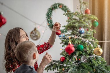 Anne ve çocuğu Noel ağacını oyuncaklar ve toplarla süslüyorlar. Yeni yıla aile hazırlığı, rahat atmosfer ve şenlik havası kavramı.