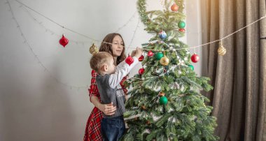 Anne ve çocuğu Noel ağacını oyuncaklar ve toplarla süslüyorlar. Yeni yıla aile hazırlığı, rahat atmosfer ve şenlik havası kavramı.