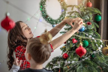 Anne ve çocuğu Noel ağacını oyuncaklar ve toplarla süslüyorlar. Yeni yıla aile hazırlığı, rahat atmosfer ve şenlik havası kavramı.