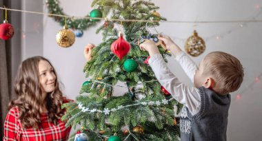 Anne ve çocuğu Noel ağacını oyuncaklar ve toplarla süslüyorlar. Yeni yıla aile hazırlığı, rahat atmosfer ve şenlik havası kavramı.