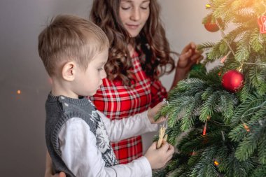 Anne ve çocuğu Noel ağacını oyuncaklar ve toplarla süslüyorlar. Yeni yıla aile hazırlığı, rahat atmosfer ve şenlik havası kavramı.