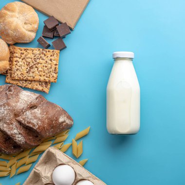 Mavi arka plan manzaralı taze yiyecekler. Ekmek, çikolata, makarna, yumurta ve bir şişe süt. Ev teslimatlı ürün kavramı.