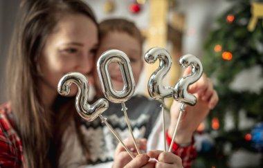 Bir Noel ağacının arka planındaki mutlu anne ve oğul ellerinde çubuklardaki 2022 gümüş rakamlarını tutuyorlar. Yeni yıl kavramı, şenlikli atmosfer, ev dekorasyonu, tebrikler..