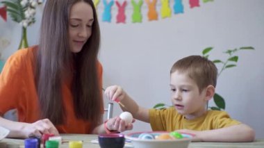 Anne ve küçük bir çocuk tatil için dekore edilmiş bir odada birlikte yumurta boyuyorlar. Aileyi Paskalya, bahar havasına hazırlama kavramı