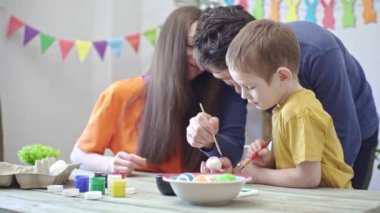 Mutlu aile, süslü bir odada Paskalya yumurtalarını boyayıp eğleniyor. Anne, baba ve çocuk tatil için hazırlanın.