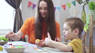 Anne ve oğlu tatil için dekore edilmiş bir odada yumurta boyuyorlar. Paskalya için aile hazırlığı kavramı, neşeli bahar havası