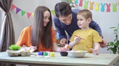 Mutlu aile dekore edilmiş bir odada Paskalya yumurtalarını boyuyor. Baba, anne ve çocuk Paskalya için hazırlık, neşeli bahar havası.