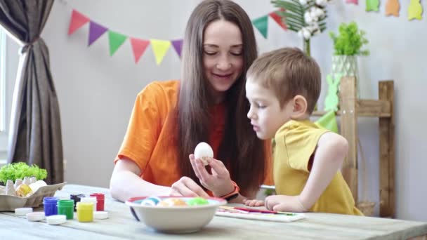 Mamá y un hijo están pintando huevos juntos en una habitación decorada para las vacaciones. Concepto de preparación familiar para la Pascua, humor festivo de primavera — Vídeo de stock