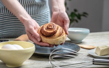 Mavi önlüklü kadın taze tarçınlı çörekleri yemek tepsisinden alıp tabağa koyuyor. Lezzetli ev yapımı hamur işleri ve rahat atmosfer kavramı.