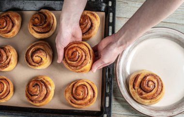 Dişi eller taze tarçınlı ruloları pişirme tepsisinden tabağa dikkatlice taşıyor. Lezzetli ev yapımı hamur işleri ve sıcak bir atmosfer kavramı. Üst görünüm.