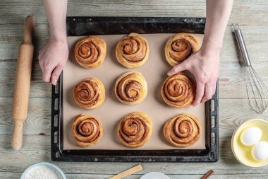 Kadın elleri dikkatle fırın tepsisinden taze tarçınlı çörekleri çıkarıyor. Lezzetli ev yapımı hamur işi ve rahat atmosfer kavramı.