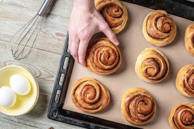 Kadın elleri dikkatle fırın tepsisinden taze tarçınlı çörekleri çıkarıyor. Lezzetli ev yapımı hamur işi ve rahat atmosfer kavramı.