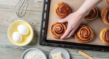 Kadın elleri dikkatle fırın tepsisinden taze tarçınlı çörekleri çıkarıyor. Lezzetli ev yapımı hamur işi ve rahat atmosfer kavramı.