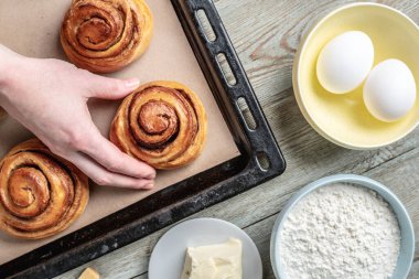 Kadın elleri dikkatle fırın tepsisinden taze tarçınlı çörekleri çıkarıyor. Lezzetli ev yapımı hamur işi ve rahat atmosfer kavramı.