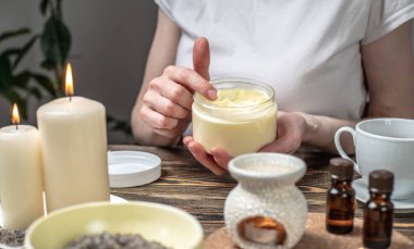 Kadın masaj yaparken ellerini doğal organik kremle sarıyor. Aroma lambası. Masada gerekli yağlar ve mumlar var. Cilt ve kendine bakım kavramı, uyum ve rahatlama atmosferi