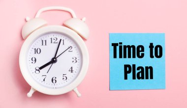 Açık pembe bir arka planda, beyaz bir çalar saat ve üzerinde Time to Plan yazan mavi bir sayfa.