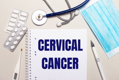 Açık gri bir arka planda, açık mavi tek kullanımlık yüz maskesi, bir stetoskop, bir elektronik termometre, haplar, bir kalem ve CERVICAL CANCER yazılı bir defter. Tıbbi konsept