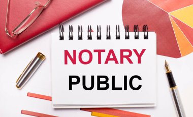 Masaüstünde NOTARY PUBLIC yazılı beyaz bir defter, bir kalem, bordo ve kırmızı masalar ve altın çerçeveli gözlük var. İş konsepti.