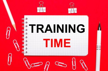 Kırmızı arka planda, beyaz bir kalem, beyaz ataçlar, beyaz bir kurşun kalem ve mesaj zamanı yazılı bir defter. Yukarıdan görüntüle