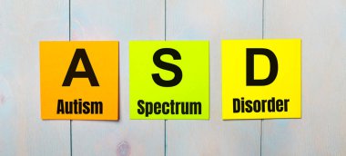 Üzerinde ASD Otizm Spektrum Bozukluğu olan üç renkli çıkartma açık mavi ahşap bir arkaplan