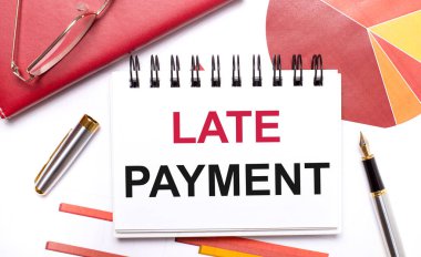 Masaüstünde beyaz bir defter var. Late PaYMENT, bir kalem, bordo ve kırmızı masalar ve altın çerçeveli gözlükler. İş konsepti.