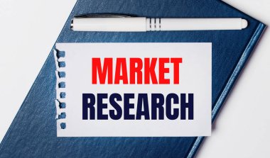 Mavi günlük arka planda yatıyor. Üzerinde beyaz bir kalem ve üzerinde MARKET RESEARCH yazılı bir kağıt parçası var