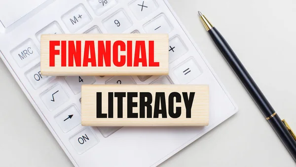 FINANCIAL LITERACY yazılı ahşap bloklar beyaz bir hesap makinesinin arka planında yatmaktadır. Yakınlarda siyah bir kol var. İş konsepti