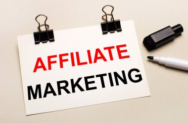 Açık bir arkaplanda, siyah bir işaretleyici ve siyah raptiyeler üzerinde beyaz bir kağıt ile AFFILIATE MARKETING