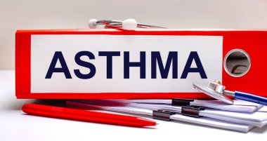 Masaüstünde steteskop, dokümanlar, kalem ve ASTHMA metninin olduğu kırmızı bir dosya klasörü var. Tıbbi konsept