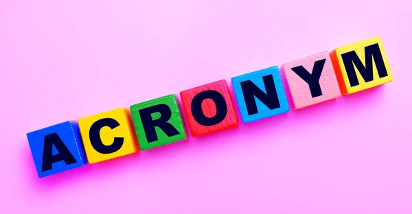 薄いピンクの背景には Acronymというテキストを持つ多色の木製のキューブ — ストック写真