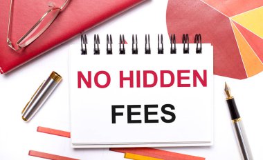 Masaüstünde beyaz bir defter var. İçinde HAYIR gizli ödemeler, bir kalem, bordo ve kırmızı masalar ve altın çerçeveli gözlükler var. İş konsepti.