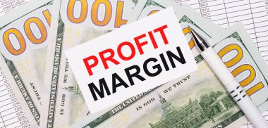 Raporların ve dolarların arka planına karşı beyaz bir kalem ve içinde PROFIT MARGIN yazan bir kart. İş konsepti