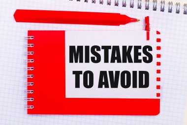 Beyaz bir not defterinde, kırmızı bir kalem, kırmızı bir not defteri ve AVOID 'e yanlış yazılmış beyaz bir sayfa.