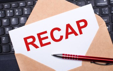 Üzerinde RECAP yazan beyaz kart çalışma masasının üstündeki el işi zarfında modern bir dizüstü bilgisayar klavyesi ve bordo kalemle birlikte. İş yerinin düz düzeni.