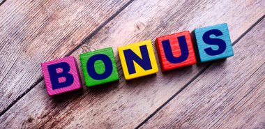 Koyu, ahşap bir arka planda, BONUS yazısıyla çok renkli, parlak tahta küpler.
