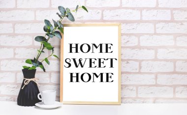 Beyaz bir masada, hafif tuğladan bir duvara karşı, koyu renkli bir vazoda bir okaliptüs dalı, beyaz bir bardak ve üzerinde 