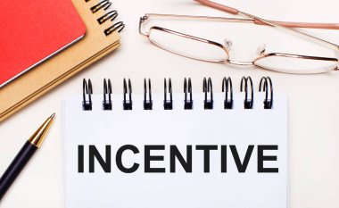 Hafif arkaplanda altın çerçeveli gözlükler, bir kalem, kahverengi ve kırmızı not defterleri ve içinde INCENTIVE yazan beyaz bir defter. İş konsepti