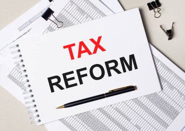 Masaüstünde dokümanlar, kalem, siyah ataçlar ve üzerinde TAX REform yazan bir defter var. İş konsepti