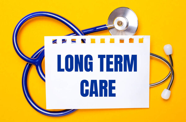 On a bright yellow background, a blue stethoscope and a sheet of paper with the text LONG TERM CARE. Medical concept