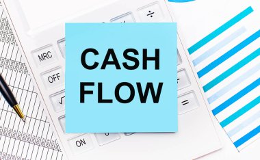 Masaüstünde CASH FLOW yazılı mavi etiketli beyaz bir hesap makinesi var, bir kalem ve mavi raporlar. İş konsepti