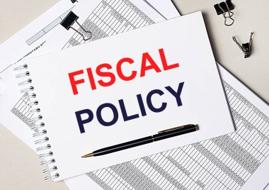 Masaüstünde belgeler, kalem, siyah ataçlar ve içinde FISCAL POLICY metni olan bir defter var. İş konsepti