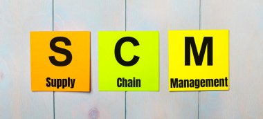 SCM Tedarik Zinciri Yönetimi yazılı üç renkli çıkartma açık mavi ahşap bir arkaplan